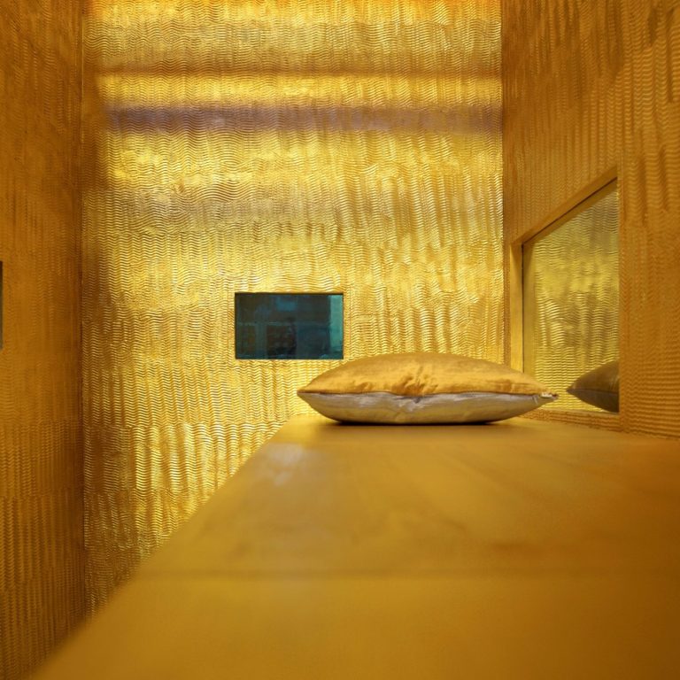 Le Pavillon du Sommeil Intérieur minimaliste avec un coussin sur une étagère et des murs dorés.